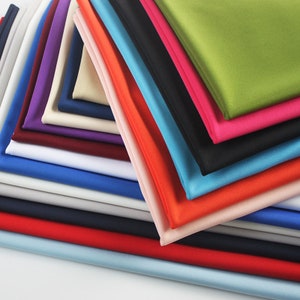May include: A stack of fabric swatches in various colours, including red, blue, green, and purple. The swatches are arranged in a layered fashion, with the top swatch being green and the bottom swatch being blue.