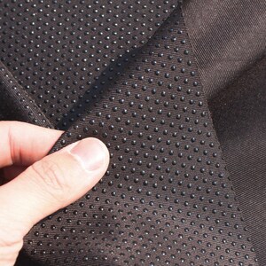 May include: Close-up of a brown fabric with a textured pattern of small black dots. The fabric is folded over, revealing a smooth side.