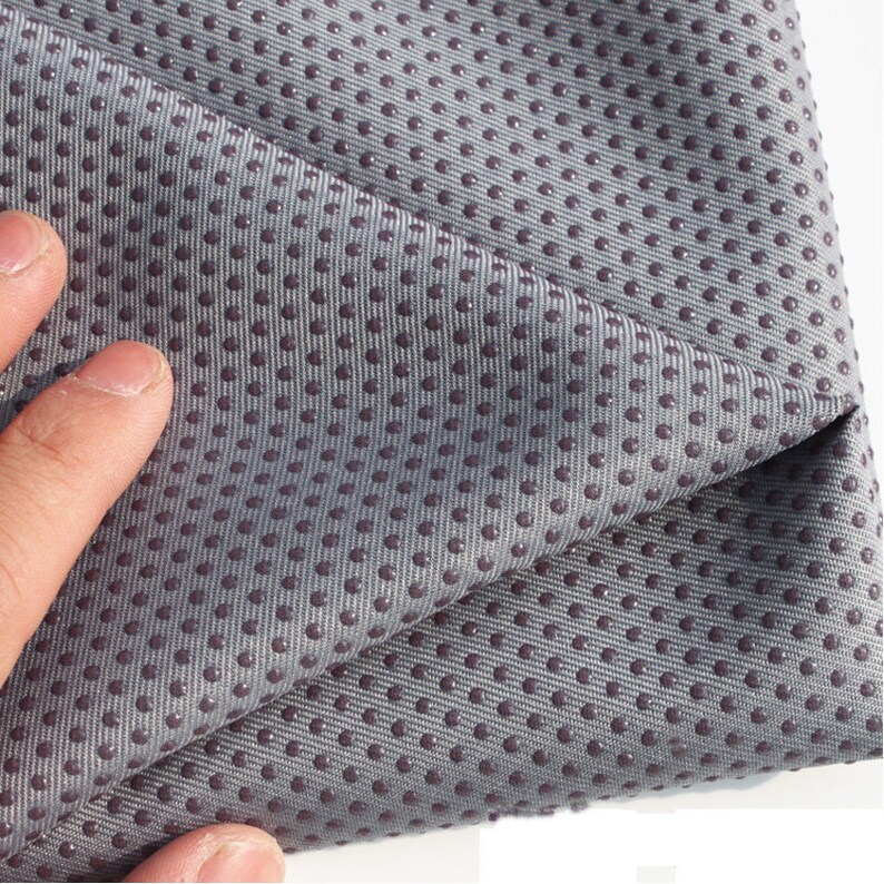 May include: Close-up of a gray yoga mat with a textured surface. The mat has small, raised dots that provide grip.