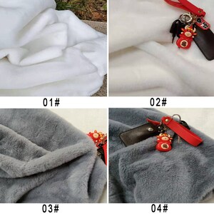 May include: Four fabric swatches, two white and two gray. The white swatches are smooth and the gray swatches are fuzzy. The top two swatches have a red and gold keychain with a small red ox charm.