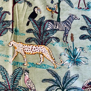 Puede incluir: Una tela verde claro con un estampado de temática selvática. El diseño incluye un leopardo amarillo y marrón, una cebra y varias aves como tucanes y loros, ambientados entre palmeras y otras plantas tropicales.