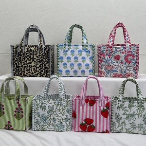 May include: Seven square tote bags with two handles each, featuring various patterns including leopard print, blue floral, red floral, green floral, blue botanical, pink and white stripes with strawberries, and green botanical prints.