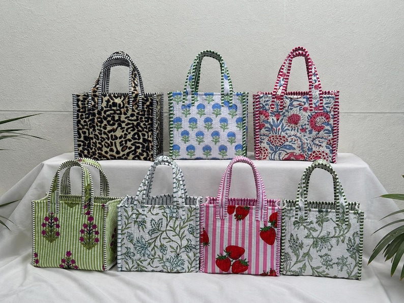 May include: Seven square tote bags with two handles each, featuring various patterns including leopard print, blue floral, red floral, green floral, blue botanical, pink and white stripes with strawberries, and green botanical prints.