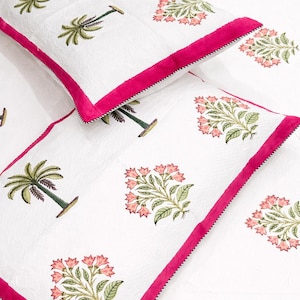 Peut inclure: Ensemble de literie blanc avec une bordure rose et des motifs floraux et de palmiers. L'ensemble comprend un oreiller et une couverture pliée, tous deux avec le même motif. Le motif floral est dans les tons de rose et de vert.