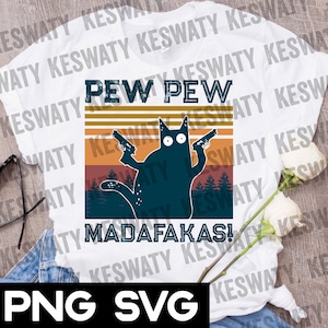 May include: White t-shirt featuring a cartoon cat holding two guns, with the words "PEW PEW MADAF*KAS!". The design includes a retro sunset background and forest silhouette. The shirt is made of a soft, comfortable material.