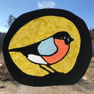 May include: A colourful paper craft of a robin bird with a black outline, set against a yellow background. The bird has a red breast, a blue belly, and a white stripe on its wing.