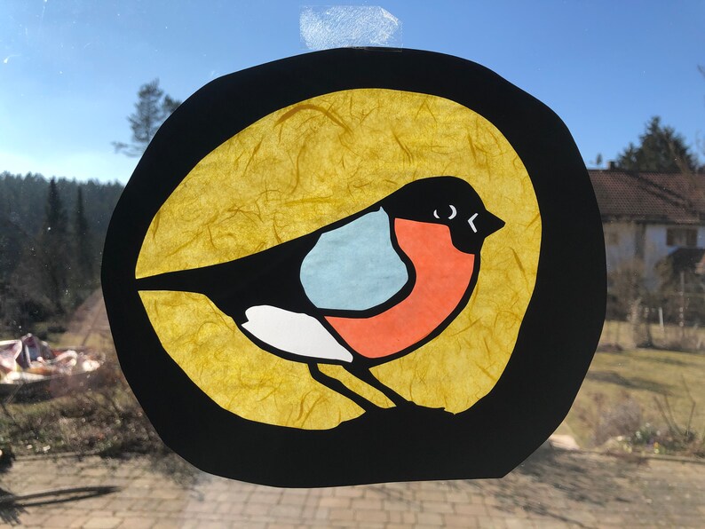 May include: A colourful paper craft of a robin bird with a black outline, set against a yellow background. The bird has a red breast, a blue belly, and a white stripe on its wing.