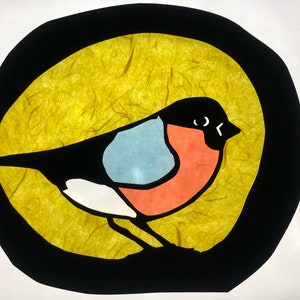 May include: A colourful paper cutout of a bird with a black body, white chest, blue wing, and red breast. The bird is set against a yellow background inside a black circle.