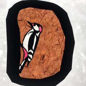 Pode incluir: Ilustra&ccedil;&atilde;o estilizada de um pica-pau. A ave &eacute; retratada em preto, branco e rosa, contra um fundo castanho texturizado dentro de uma borda preta. A obra de arte tem um estilo gr&aacute;fico simples.