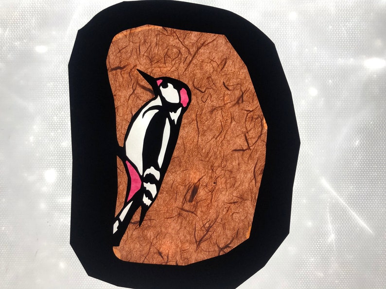 Pode incluir: Ilustra&ccedil;&atilde;o estilizada de um pica-pau. A ave &eacute; retratada em preto, branco e rosa, contra um fundo castanho texturizado dentro de uma borda preta. A obra de arte tem um estilo gr&aacute;fico simples.