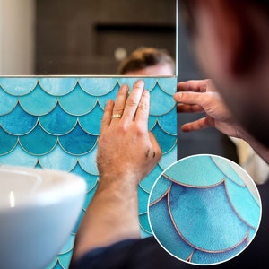 Puede incluir: Una persona está aplicando un papel de contacto con un patrón de escamas de sirena azul y dorado a un espejo. El papel de contacto tiene un efecto acuarela sutil.