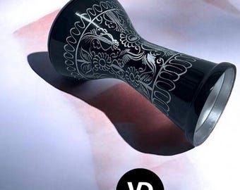 May include: A black goblet drum featuring intricate silver floral engravings across its surface. The drum has a wide, flared top and a narrower base, with a metallic silver interior rim visible at the bottom opening. A circular logo reads VD VATAN since 1975.