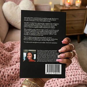 Puede incluir: Un libro negro titulado "How Work Actually Works" se sostiene frente a un fondo rosa. La portada del libro presenta texto blanco y una foto de una mujer. La contraportada del libro tiene texto y un código de barras.