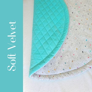 May include: A turquoise soft velvet play mat with a white and gray patterned underside. The mat is quilted and has a rounded edge.