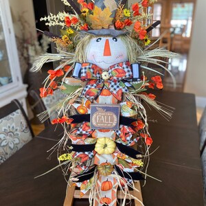 Peut inclure: Une d&eacute;coration de porte d'automne sur le th&egrave;me de l'&eacute;pouvantail avec une base en toile de jute et en paille, un visage en tissu avec un n&oelig;ud et une pancarte qui dit "I think I love FALL most of all".