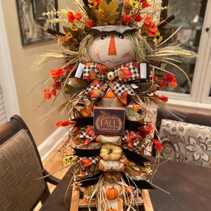 Peut inclure: Une d&eacute;coration de scarecrow sur le th&egrave;me de l'automne avec un visage en toile de jute, un n&oelig;ud &agrave; carreaux noir et blanc et une pancarte qui dit "Je pense que j'aime l'automne plus que tout". Le scarecrow est d&eacute;cor&eacute; de citrouilles, de feuilles d'automne et d'autres accents sur le th&egrave;me de l'automne.