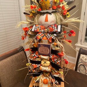 Peut inclure: Une d&eacute;coration de scarecrow sur le th&egrave;me de l'automne avec un chapeau en toile de jute, un ruban &agrave; carreaux et noir, et une pancarte qui dit "Je pense que j'aime l'automne plus que tout".