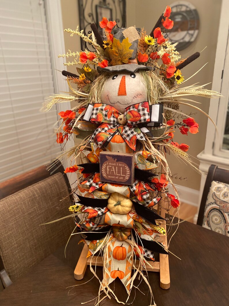 Peut inclure: Une d&eacute;coration de scarecrow sur le th&egrave;me de l'automne avec un chapeau en toile de jute, un ruban &agrave; carreaux et noir, et une pancarte qui dit "Je pense que j'aime l'automne plus que tout".