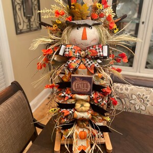 Peut inclure: Une d&eacute;coration d'automne sur le th&egrave;me de l'&eacute;pouvantail avec un visage en toile de jute, un n&oelig;ud &agrave; carreaux noir et blanc et une pancarte qui dit "Je pense que j'aime l'automne plus que tout".