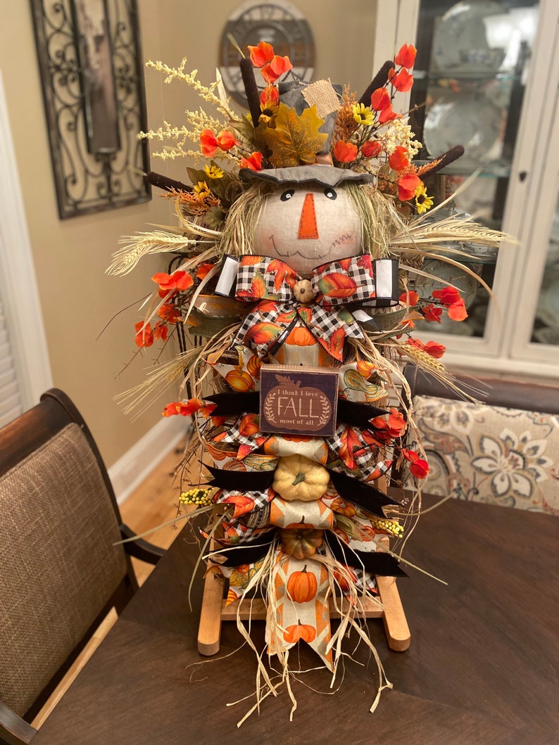 Peut inclure: Une d&eacute;coration d'automne sur le th&egrave;me de l'&eacute;pouvantail avec un visage en toile de jute, un n&oelig;ud &agrave; carreaux noir et blanc et une pancarte qui dit "Je pense que j'aime l'automne plus que tout".