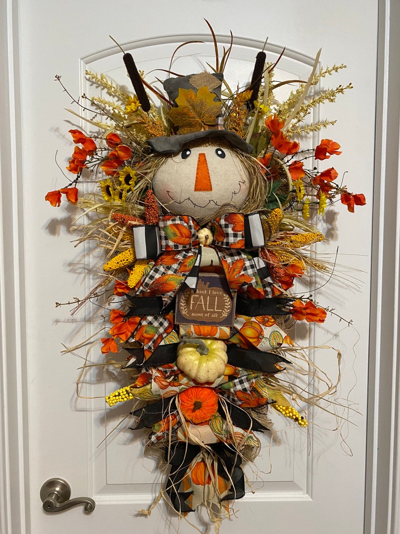 Peut inclure: Une couronne de porte sur le th&egrave;me de l'automne avec un visage de  &eacute;pouvantail, un n&oelig;ud &agrave; carreaux noir et blanc et une pancarte qui dit "Je pense que j'aime l'automne plus que tout".
