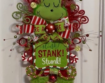May include: A green Grinch Christmas wreath with a red and white striped bow, a sign that says "You're a Mean One, Mr. Grinch! A Stink! Stank! Stunk!" and a green fuzzy bow.