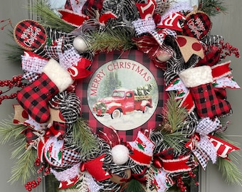 May include: A red, black, and white Christmas wreath with a red truck and "Merry Christmas" sign in the center. The wreath is decorated with plaid ribbon, white and black buffalo check fabric, red berries, and white ornaments.