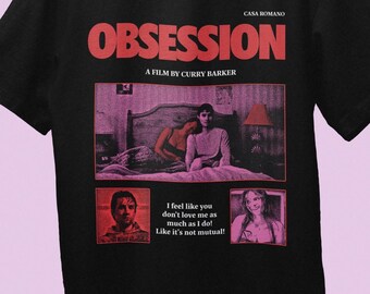 Könnte beinhalten: Ein schwarzes T-Shirt mit einem roten Grafikdruck mit dem Text "CASA ROMANO", "OBSESSION" und "A FILM BY CURRY BARKER". Das Design zeigt eine zentrale Szene mit zwei Personen in einem Schlafzimmer und zwei Porträts mit dem Text "I feel like you don't love me as much as I do! Like it's not mutual!"