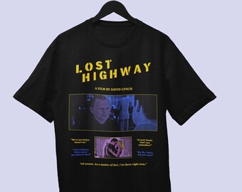 Könnte beinhalten: Ein schwarzes Kurzarm-T-Shirt mit dem gelben Schriftzug LOST HIGHWAY und A FILM BY DAVID LYNCH. Die Grafik zeigt eine blau getönte Szene mit zwei Personen, ein kleineres rechteckiges Bild eines Paares sowie Dialogtext in Gelb und Blau.