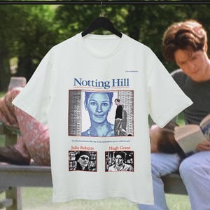 Puede incluir: Una camiseta blanca de manga corta con un estampado de la película Notting Hill. El diseño incluye el título, una imagen central de Julia Roberts y dos fotos más pequeñas de Julia Roberts y Hugh Grant con el texto: Can the most famous film star in the world fall for just an ordinary guy!