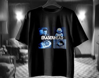 Könnte beinhalten: Ein schwarzes kurzärmeliges T-Shirt mit einem Grafikdruck aus dem Film Eraserhead. Das Design besteht aus vier bläulichen Feldern mit Filmszenen, wobei der weiße Schriftzug Eraserhead mittig über dem Druck platziert ist.