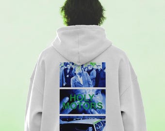 Könnte beinhalten: Ein weißer Kapuzenpullover mit einem Grafikdruck auf der Rückseite. Der Druck besteht aus drei übereinander angeordneten Feldern mit Filmszenen, wobei der grüne Text HOLY MOTORS im mittleren Feld über einem bläulichen Nahbild steht.