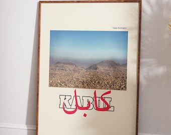 Puede incluir: Una impresión artística enmarcada con una fotografía de un paisaje urbano bajo un cielo azul. La palabra "KABUL" se muestra en texto estilizado rojo y negro. La impresión está sobre un fondo crema y enmarcada en un marco de madera marrón.