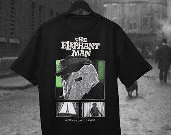 Könnte beinhalten: Ein schwarzes Kurzarm-T-Shirt mit einem Grafikdruck aus dem Film The Elephant Man. Das Design zeigt den Titel, ein Porträt der Hauptfigur mit Mütze, zwei kleinere Szenenbilder und den Schriftzug A FILM BY DAVID LYNCH.