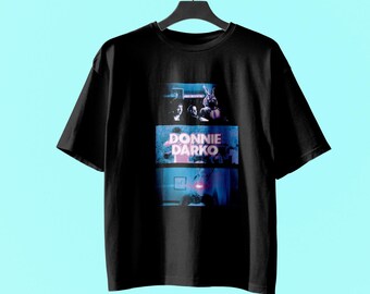Könnte beinhalten: Ein schwarzes T-Shirt mit kurzen Ärmeln und einem Grafikdruck aus drei übereinander angeordneten Feldern. Das Design zeigt Szenen aus dem Film Donnie Darko, mit dem Text DONNIE DARKO in weißen Buchstaben im mittleren Feld und einer Hasenfigur.