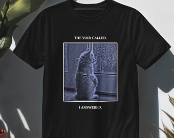 Könnte beinhalten: Ein schwarzes Kurzarm-T-Shirt mit einer quadratischen Grafik einer Katze, die aus einem Fenster schaut. Über dem Bild steht der Text THE VOID CALLED. Unter dem Bild steht der Text I ANSWERED. Die Katze ist in Blau- und Grautönen dargestellt.