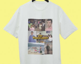Könnte beinhalten: Ein weißes Kurzarm-T-Shirt mit einer Collage aus verschiedenen Fotografien und dem Text The Wizard of Loneliness in gelber Schrift. Die Bilder zeigen Szenen mit Menschen in sozialen Umgebungen, ein Boot und ein Porträt eines Mannes.