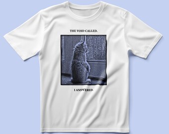 Könnte beinhalten: Ein weißes T-Shirt mit kurzen Ärmeln und einem quadratischen Aufdruck, der ein Kätzchen zeigt, das aus einem Fenster in den Regen schaut. Der Text über dem Bild lautet THE VOID CALLED. und darunter steht I ANSWERED. Der Druck ist in Blautönen.
