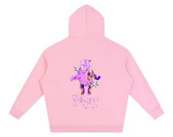 Könnte beinhalten: Ein hellrosa Kapuzenpullover mit einer Grafik auf der Rückseite. Das Design zeigt einen stilisierten Bären in Violett-, Orange- und Gelbtönen, flankiert von zwei vierzackigen Sternen. Unter dem Bären steht das Wort "Believe" in einer stilisierten Schrift.