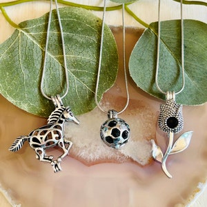 May include: Three silver necklaces with different charms. The charms are a giraffe, a soccer ball, and a flower. The necklaces are on a light brown background.
