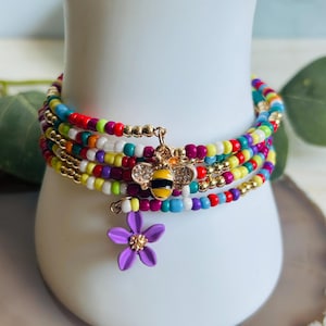 Peut inclure: Bracelet multi-rangs de perles colorées avec un charme abeille et fleur. Le bracelet est composé de petites perles colorées et a un charme abeille doré avec un charme fleur violet.