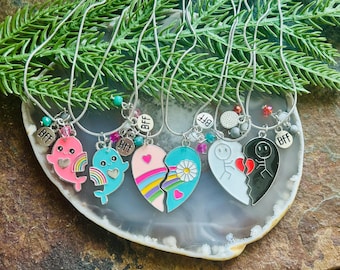 May include: A collection of silver necklaces with pendant charms. The charms include split heart designs, cartoon dolphins, and the letters "BFF". The necklaces are displayed on a decorative stone.