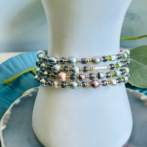 May include: A multi-strand bracelet featuring a mix of iridescent, silver, and gold beads. The bracelet is layered with different sizes and colors of beads, creating a unique and eye-catching design.