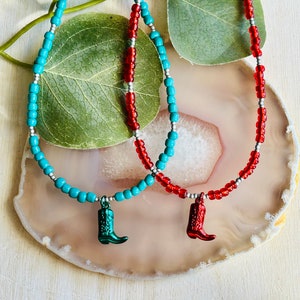 May include: Two beaded necklaces with silver accents and boot charms. One necklace is turquoise blue and the other is red.