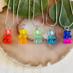 May include: Five silver chain necklaces with gummy bear pendants. The gummy bears are in different colours: orange, green, light blue, blue, and pink.