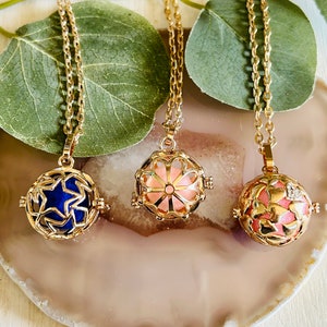 May include: Three gold necklaces with different colored charms. The charms are round and have a delicate, intricate design. The charms are blue, pink, and white.