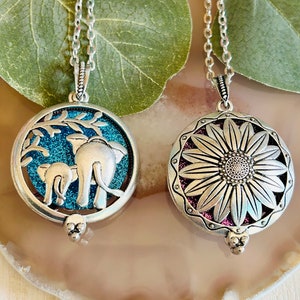 May include: Two silver pendant necklaces. One has an elephant design with a blue background, the other a sunflower design with a purple background. Both pendants hang from delicate silver chains.