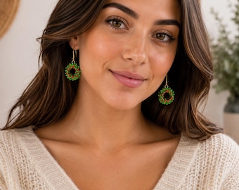 May include: A pair of drop earrings featuring circular wreaths made of small green and red beads. The earrings are suspended from gold-toned metal hooks. Each wreath is constructed from a dense cluster of tiny, vibrant green beads accented with small, bright red beads that mimic the appearance of berries on a festive wreath.