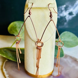 May include: A pair of rose gold earrings with a geometric triangle design and dangling strands of wire.