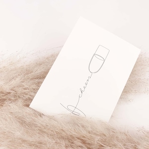May include: A white card with a black line drawing of a champagne flute and the word "cheers" written in cursive.